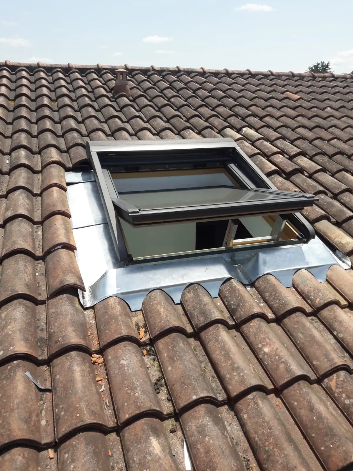 Installation d'une fenêtre de toit Velux sur une toiture en tuiles, avec des raccords en zinc pour assurer l'étanchéité