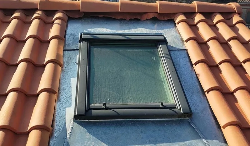 Fenêtre de toit Velux installée sur une toiture en tuiles avec une finition en zinc pour assurer l'étanchéité