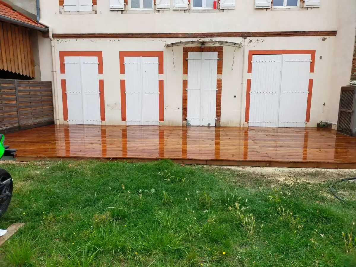 Terrasse en bois récemment installée et entretenue devant une maison avec des volets blancs fermés